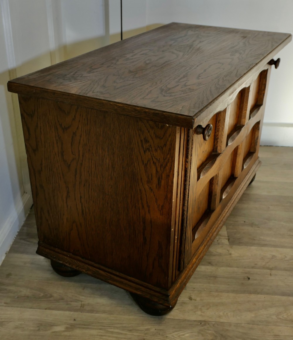 An Arts and Crafts golden oak low music cabinet with a rectangular top, six-panel fall-front door, round metal pulls, and turned feet. View IV