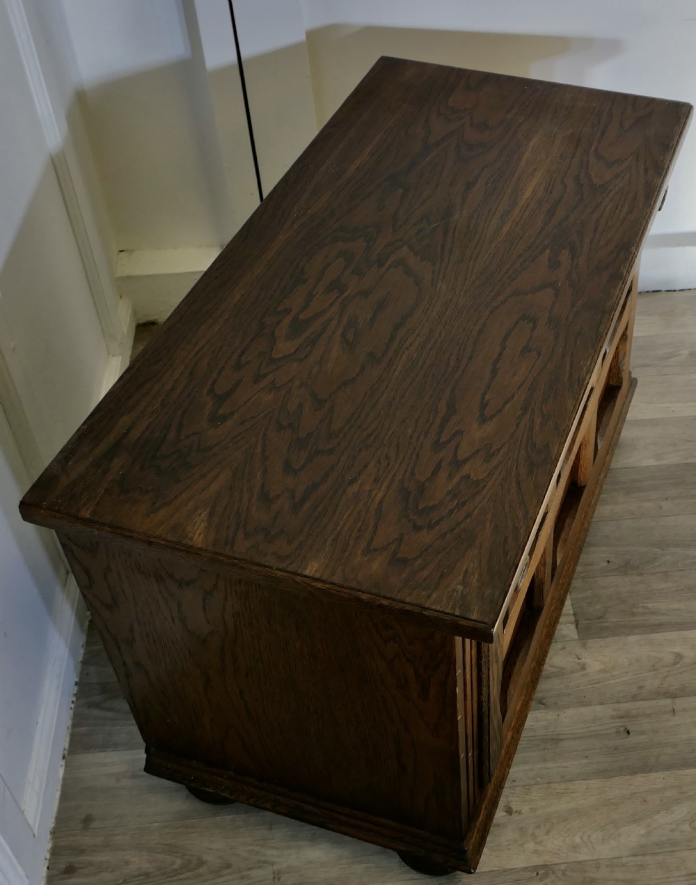 An Arts and Crafts golden oak low music cabinet with a rectangular top, six-panel fall-front door, round metal pulls, and turned feet. View V