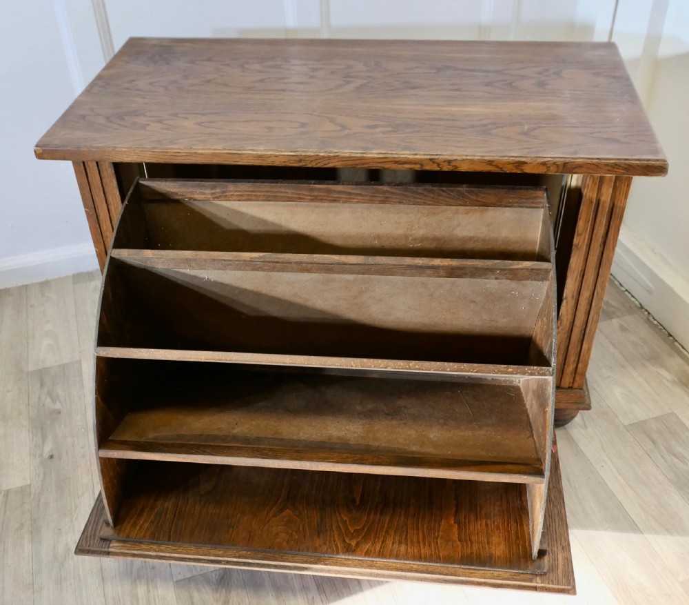 An Arts and Crafts golden oak low music cabinet with a rectangular top, six-panel fall-front door, round metal pulls, and turned feet. View VI