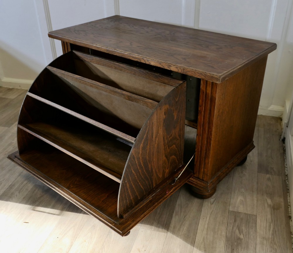 An Arts and Crafts golden oak low music cabinet with a rectangular top, six-panel fall-front door, round metal pulls, and turned feet. View VII