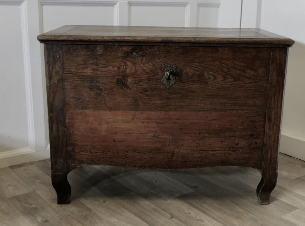 An 18th-century small dark oak French coffer featuring a flat top, central wrought iron escutcheon, and subtle cabriole legs.