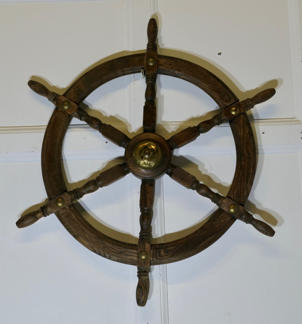 An early twentieth-century oak ship wheel featuring eight turned spokes and a central brass hub.