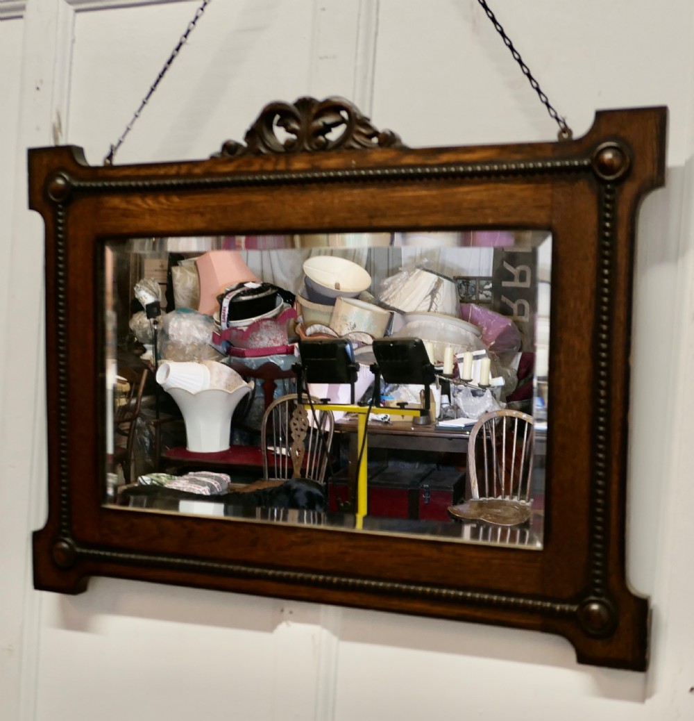 A horizontal rectangular dark oak framed mirror featuring a top carved crest, beaded inner moulding, and an attached hanging chain. View V