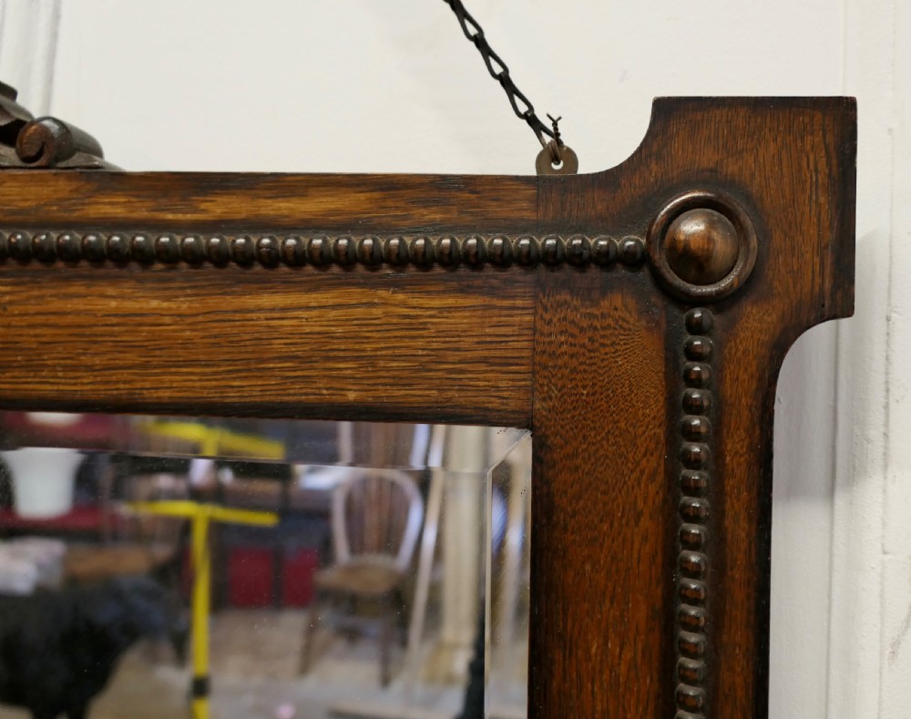 A horizontal rectangular dark oak framed mirror featuring a top carved crest, beaded inner moulding, and an attached hanging chain. View VI