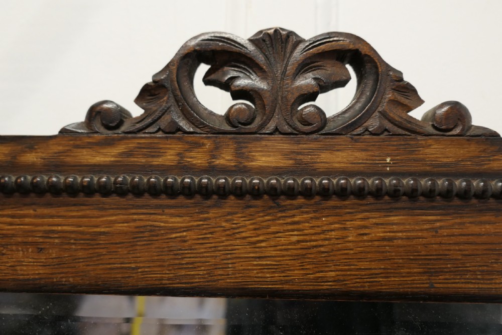 A horizontal rectangular dark oak framed mirror featuring a top carved crest, beaded inner moulding, and an attached hanging chain. View VII
