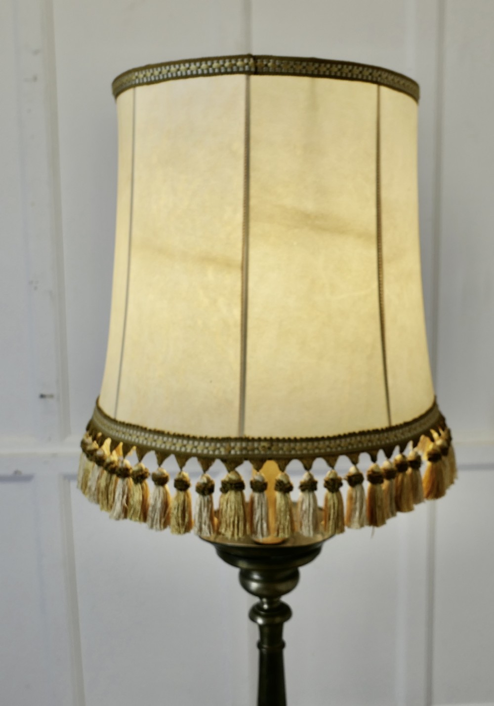 A tall brass lamp featuring a turned baluster column base paired with a cream fabric shade trimmed with tassel fringe. View VIII