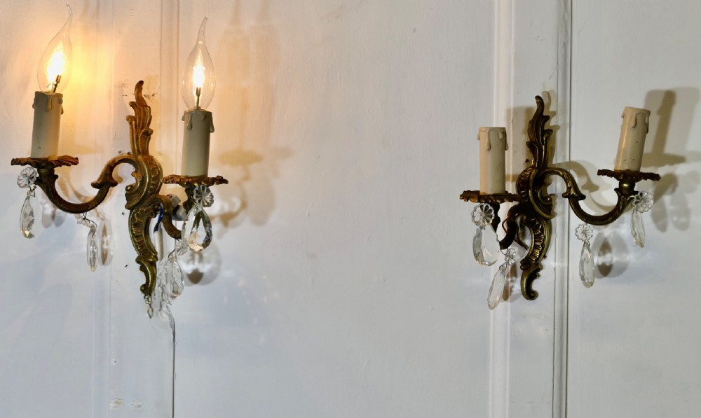 A pair of French brass twin-arm wall sconces decorated with leaf scrollwork and hanging cut-crystal glass droplets.
