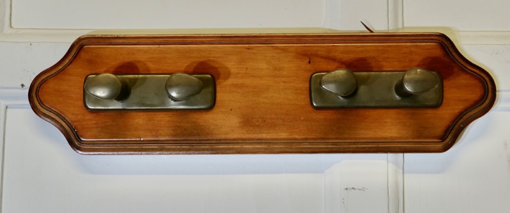 A wall-mounted shaped wooden backboard fitted with two pairs of smooth bronze nautical cleat hooks.