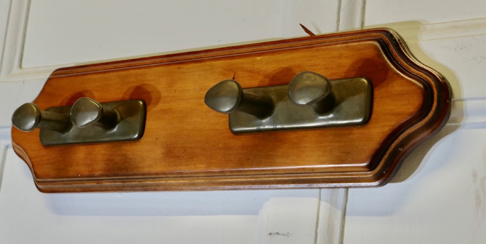 A wall-mounted shaped wooden backboard fitted with two pairs of smooth bronze nautical cleat hooks. View III