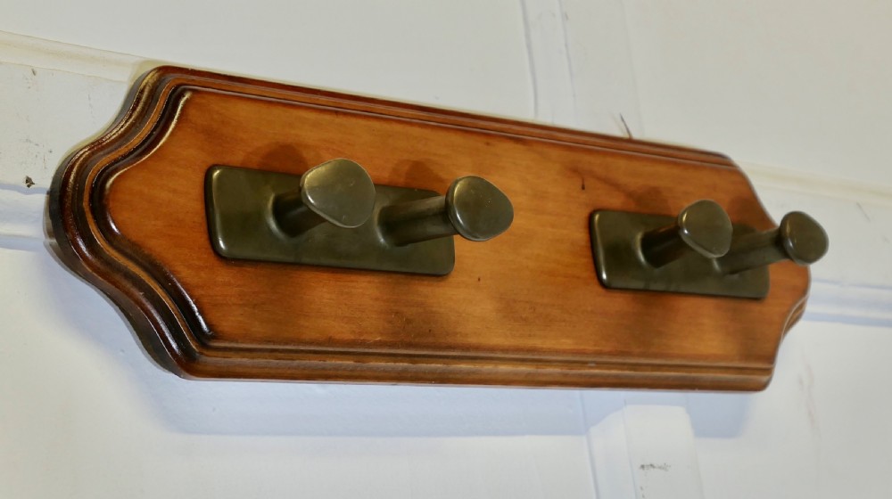 A wall-mounted shaped wooden backboard fitted with two pairs of smooth bronze nautical cleat hooks. View IV