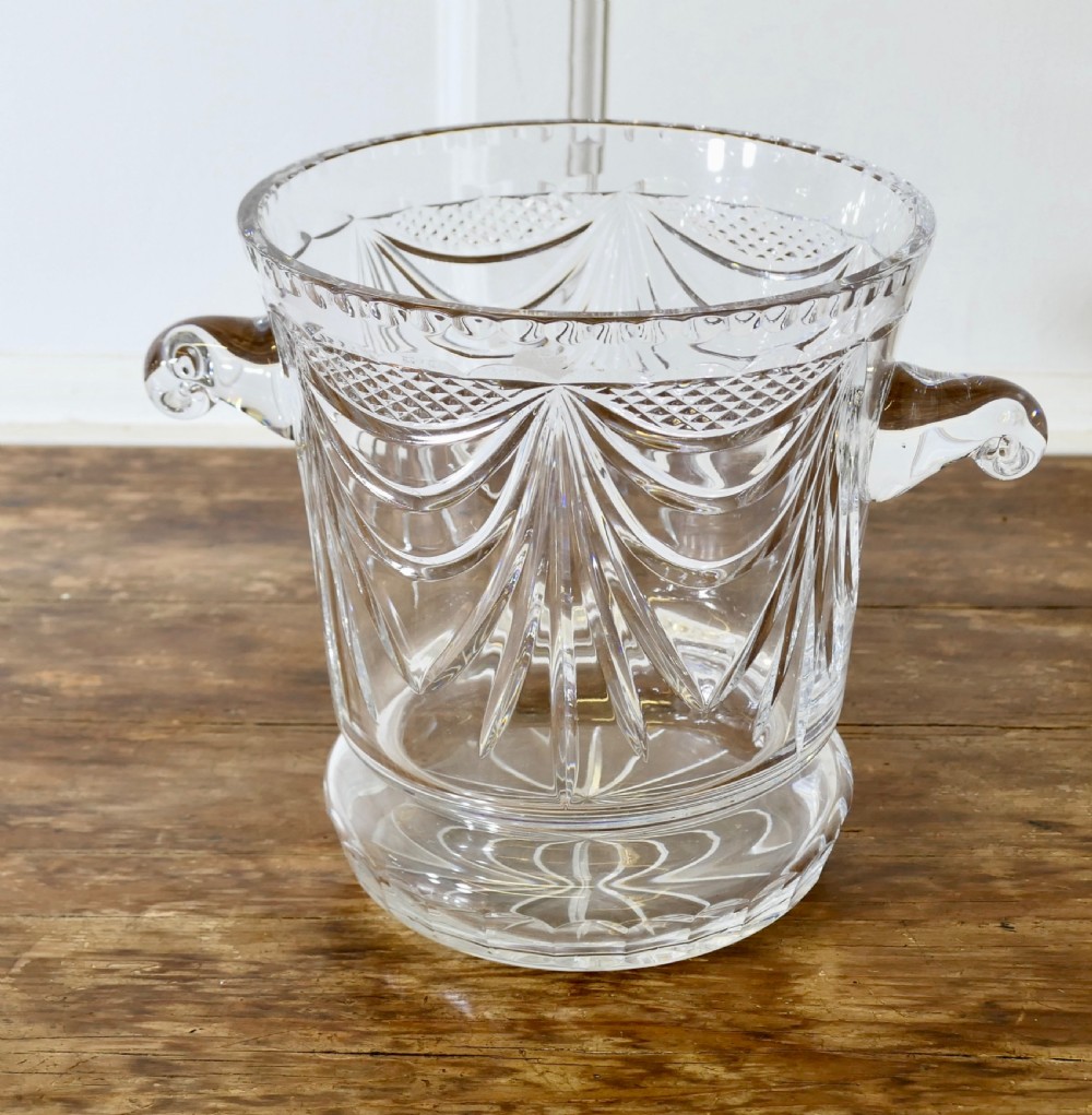 A heavy clear cut crystal champagne ice bucket featuring geometric drapery cuts, two applied scroll handles, and a stepped circular base. View II