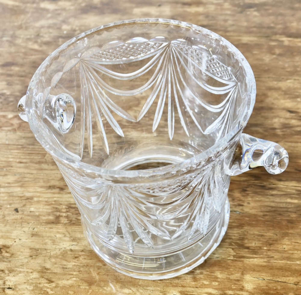 A heavy clear cut crystal champagne ice bucket featuring geometric drapery cuts, two applied scroll handles, and a stepped circular base. View III