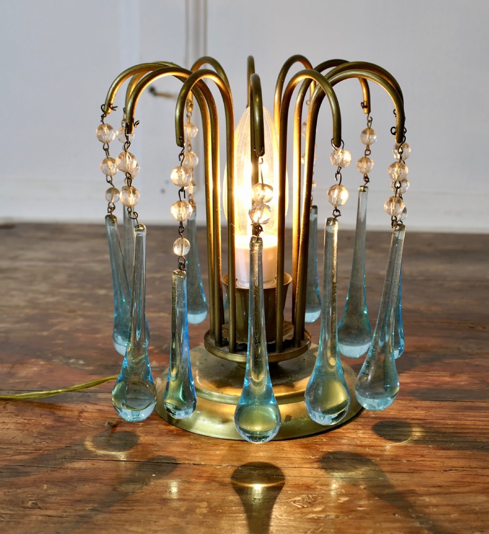 A small brass table lamp with curved radiating arms hanging clear crystal beads and light blue teardrop glass prisms around a central illuminated bulb.