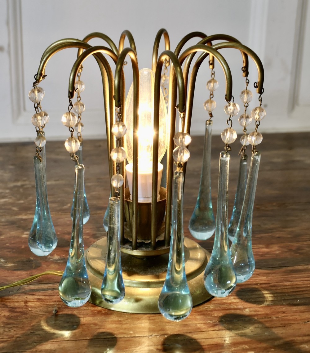 A small brass table lamp with curved radiating arms hanging clear crystal beads and light blue teardrop glass prisms around a central illuminated bulb. View III