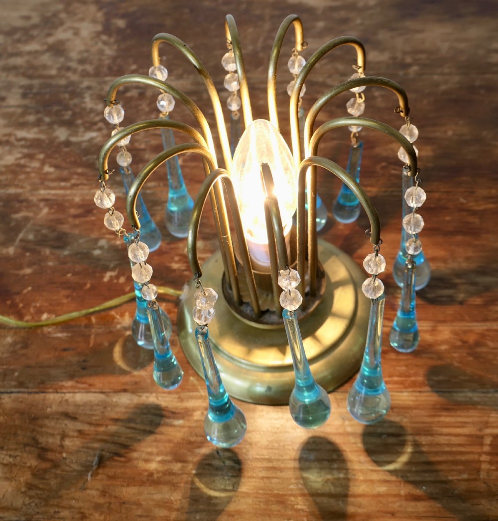 A small brass table lamp with curved radiating arms hanging clear crystal beads and light blue teardrop glass prisms around a central illuminated bulb. View V