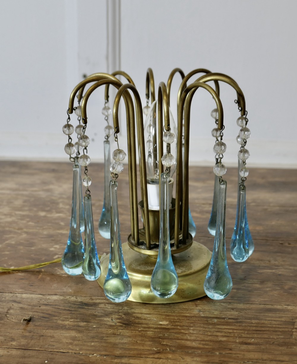 A small brass table lamp with curved radiating arms hanging clear crystal beads and light blue teardrop glass prisms around a central illuminated bulb. View VI