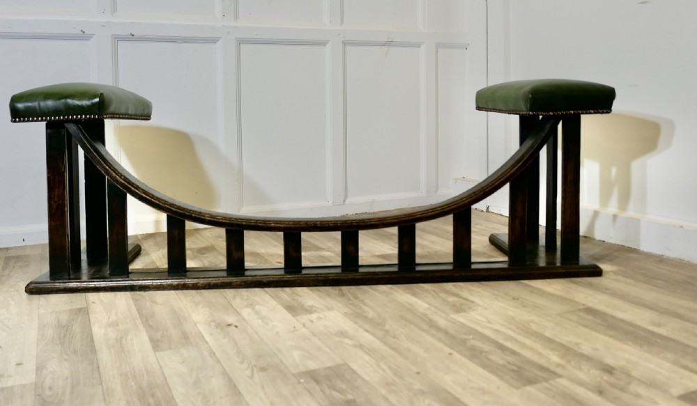 An Arts and Crafts dark oak club fender featuring two green leather upholstered seats with brass studding above vertical timber slats. View IV