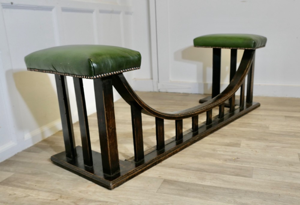 An Arts and Crafts dark oak club fender featuring two green leather upholstered seats with brass studding above vertical timber slats.