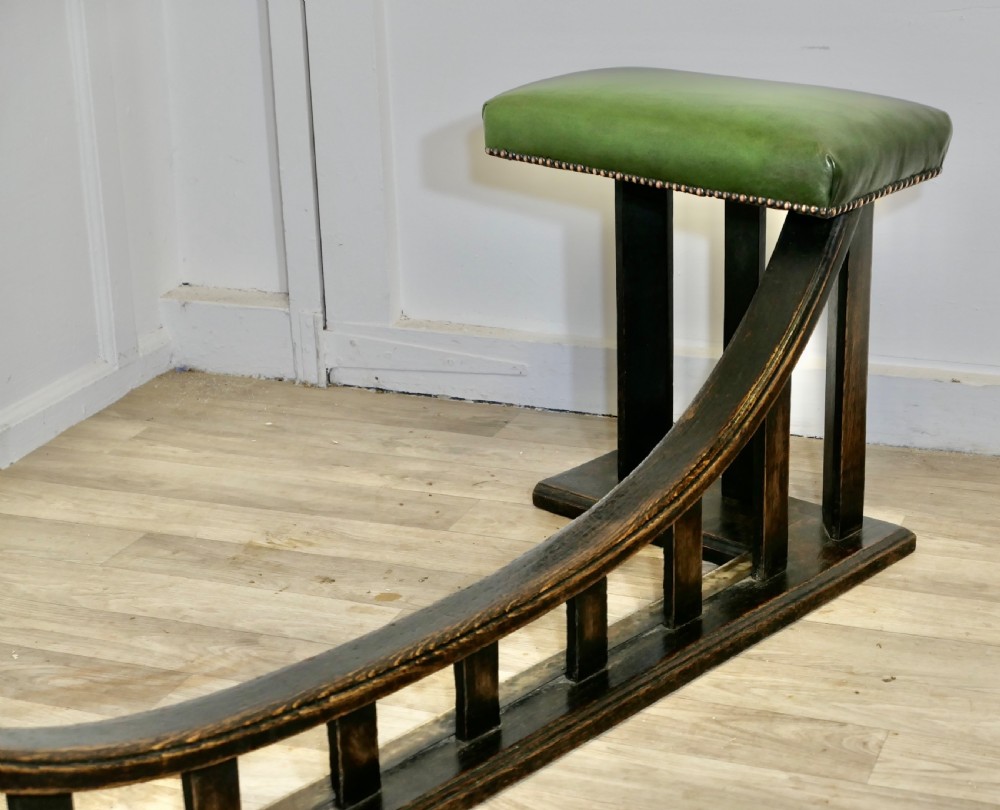 An Arts and Crafts dark oak club fender featuring two green leather upholstered seats with brass studding above vertical timber slats. View V