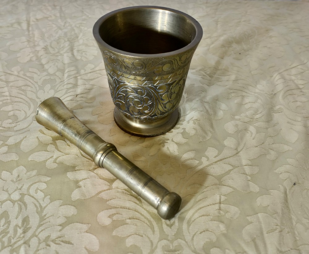 A heavy cast brass mortar decorated with intricate floral scrollwork engraving alongside a matching turned brass pestle.