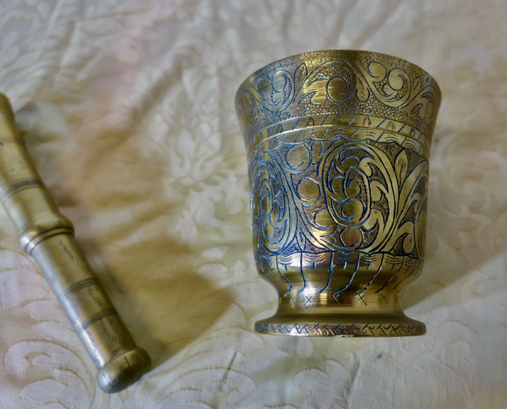 A heavy cast brass mortar decorated with intricate floral scrollwork engraving alongside a matching turned brass pestle. View IV