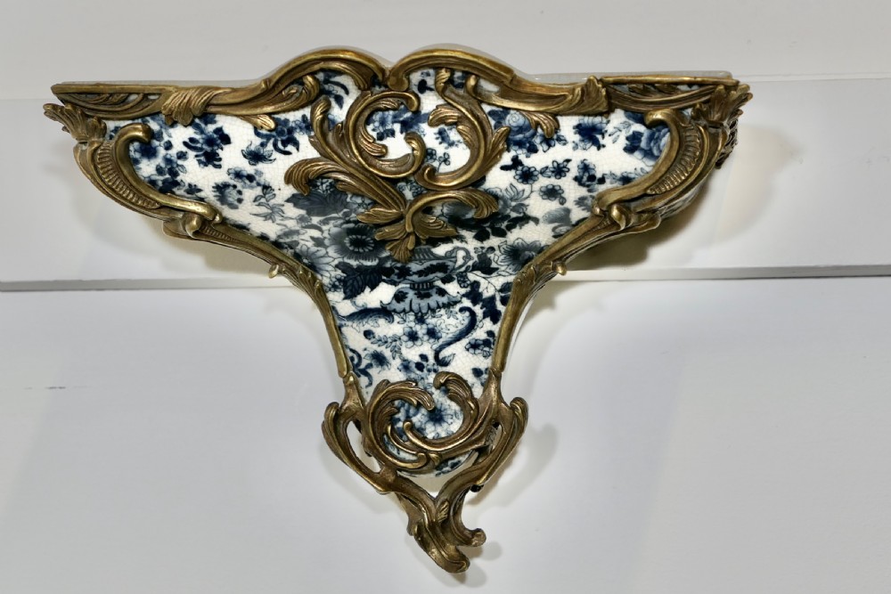 A Rococo revival wall bracket featuring blue and white floral glazed ceramic enclosed in ornamental gilt bronze foliage scrollwork. View II