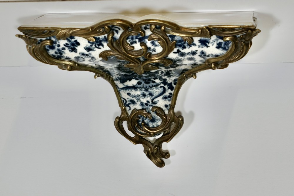 A Rococo revival wall bracket featuring blue and white floral glazed ceramic enclosed in ornamental gilt bronze foliage scrollwork. View III
