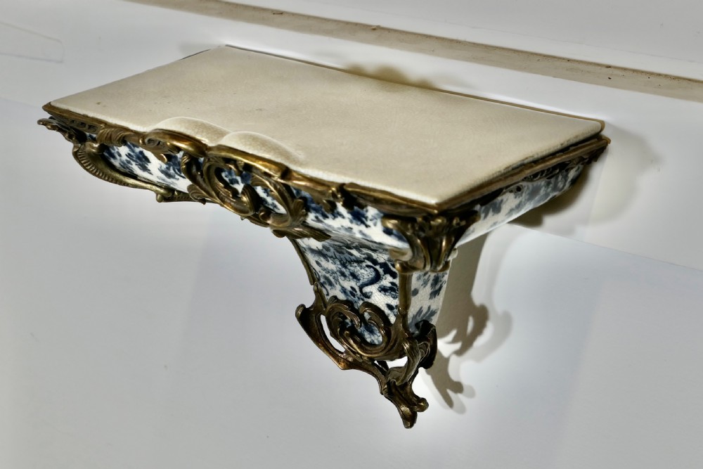 A Rococo revival wall bracket featuring blue and white floral glazed ceramic enclosed in ornamental gilt bronze foliage scrollwork. View V