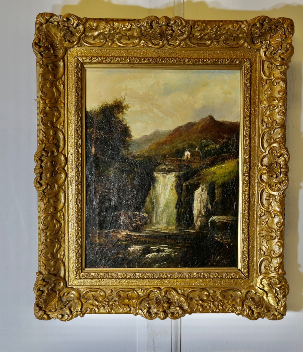 An antique Victorian oil painting depicting a cascading waterfall in a mountainous landscape, framed within an ornate gilded frame.