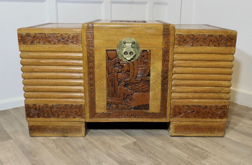 An Art Deco limed oak storage chest featuring horizontal ribbed side moulding, relief carved dragon panels, and a central brass lock plate.