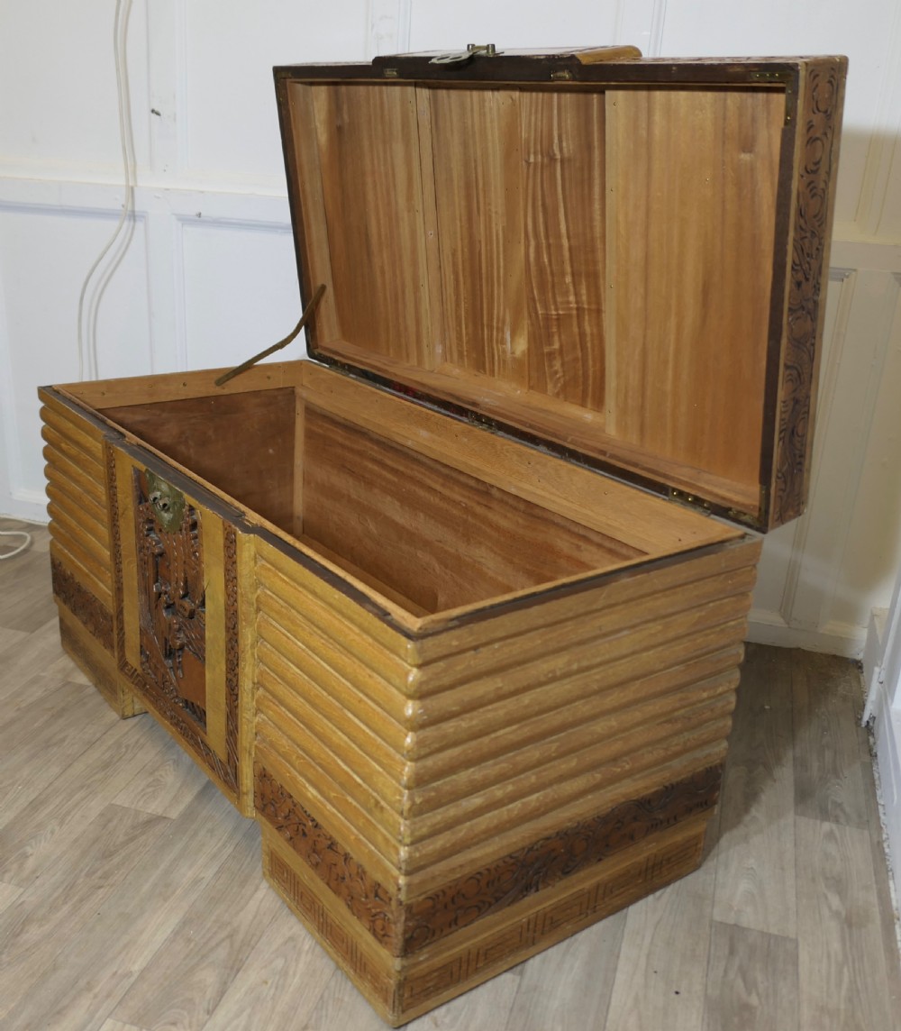 An Art Deco limed oak storage chest featuring horizontal ribbed side moulding, relief carved dragon panels, and a central brass lock plate. View II