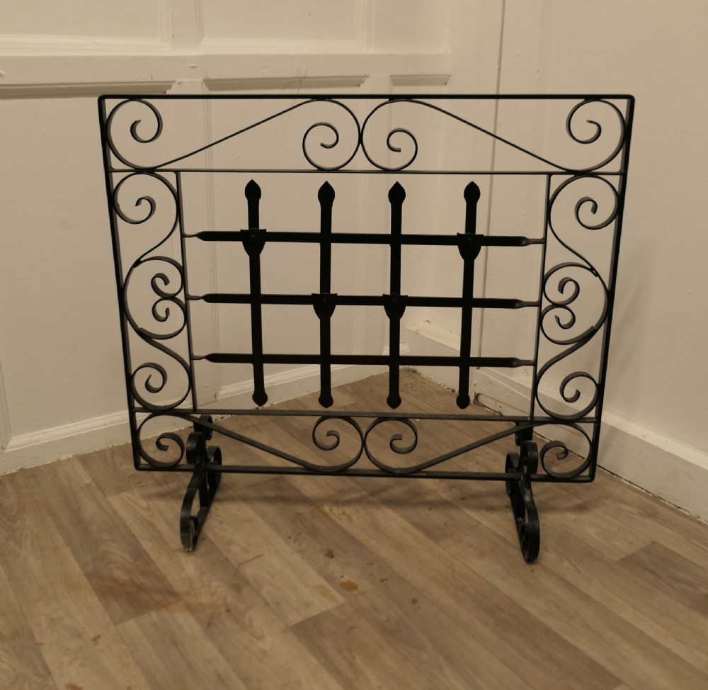 A black wrought iron fire screen featuring scrollwork borders, central vertical bars with finials, and twin scroll feet.
