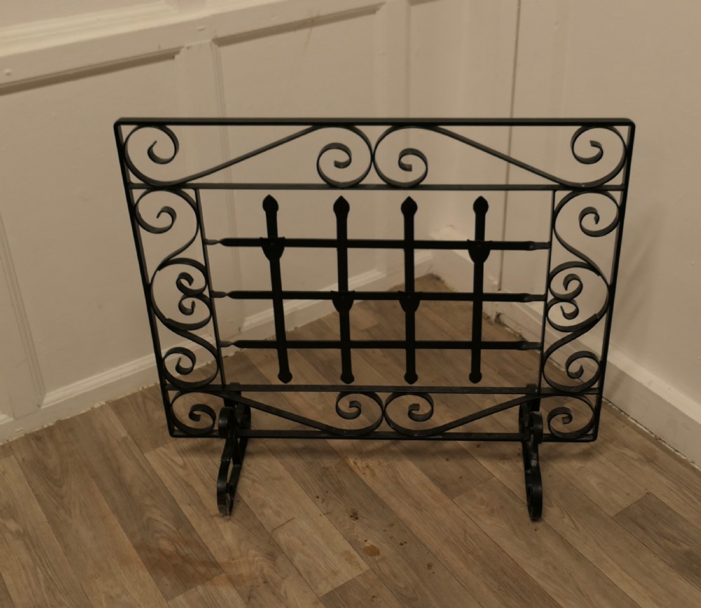 A black wrought iron fire screen featuring scrollwork borders, central vertical bars with finials, and twin scroll feet. View II
