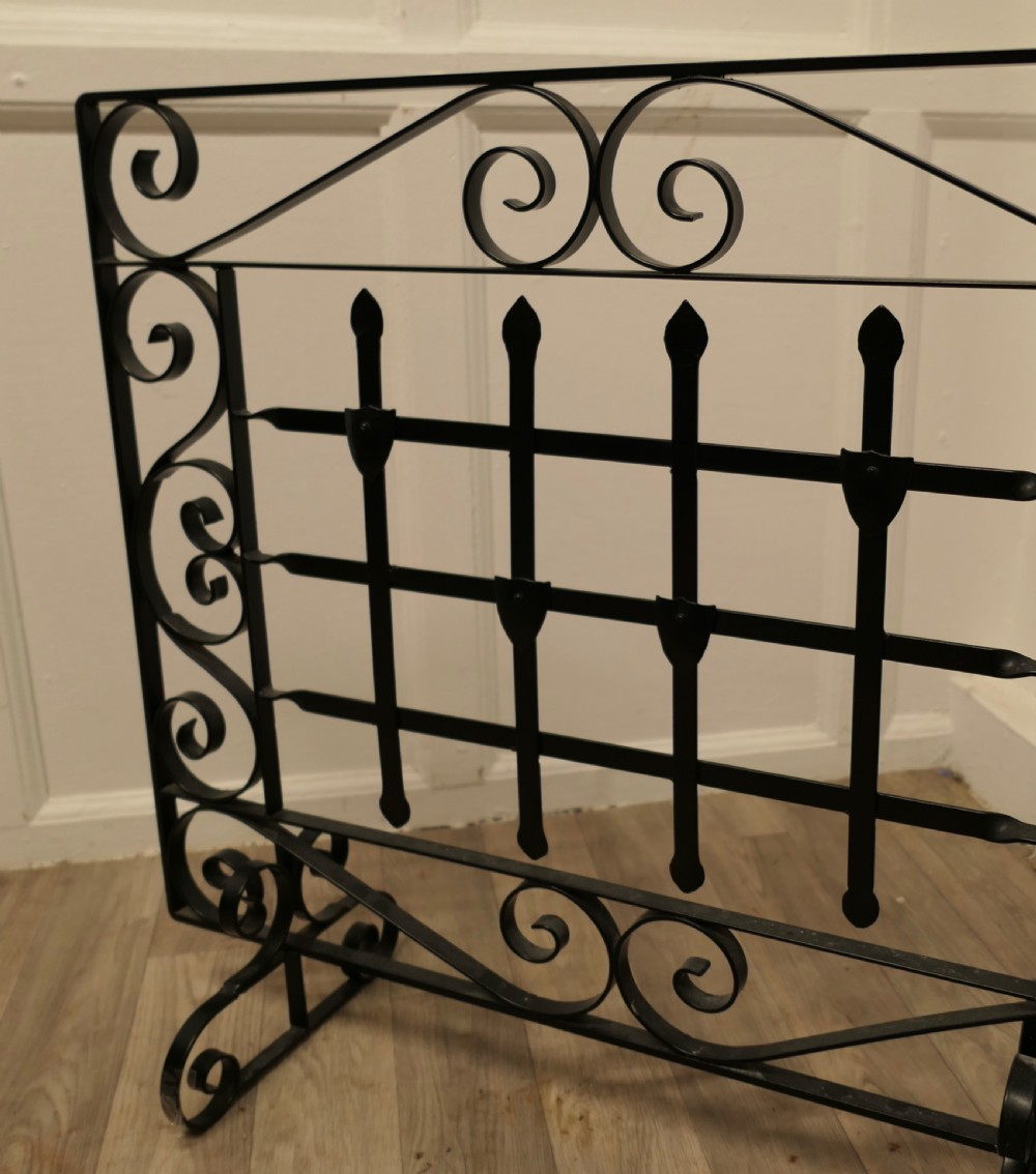 A black wrought iron fire screen featuring scrollwork borders, central vertical bars with finials, and twin scroll feet. View III