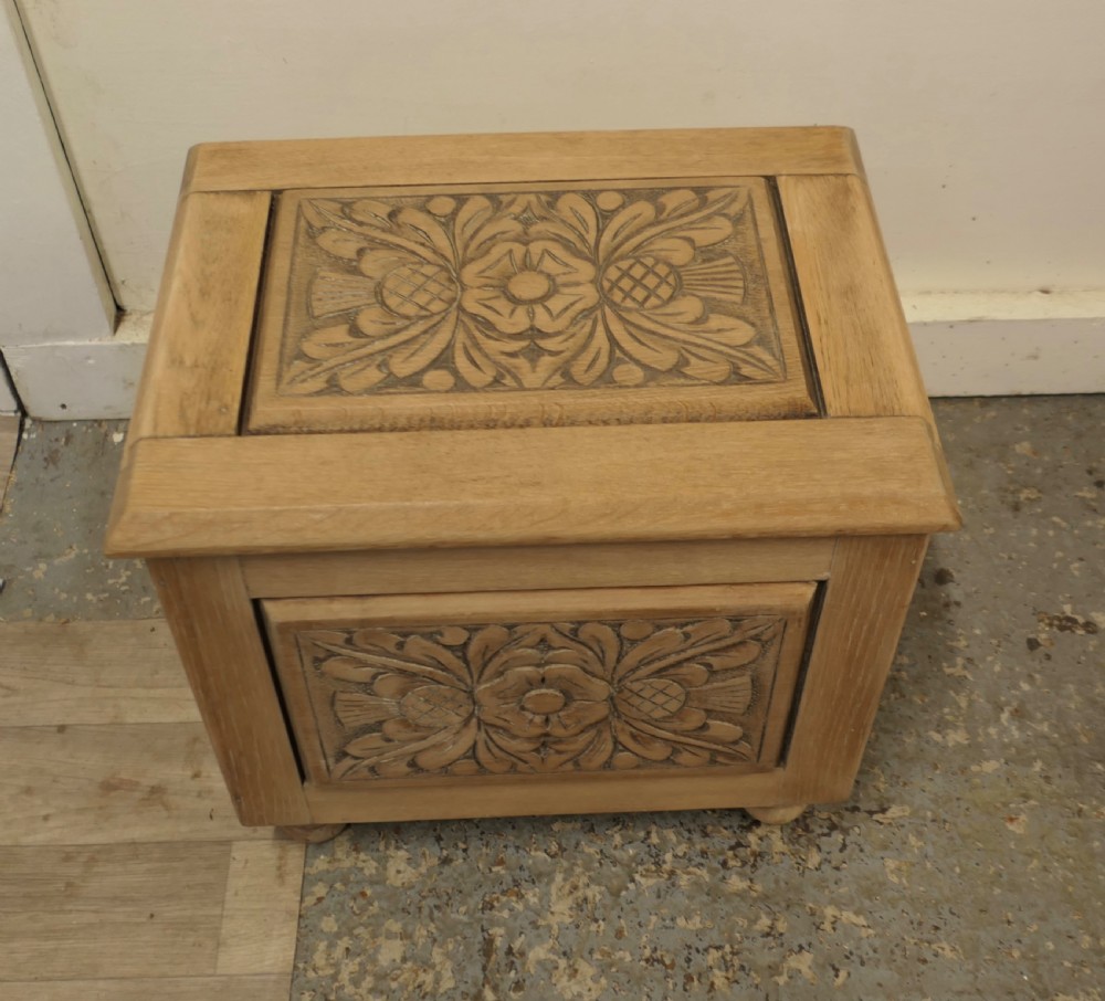 A rectangular bleached oak Arts and Crafts coal purdonium featuring a detailed floral carving on the front panel and low turned feet. View II