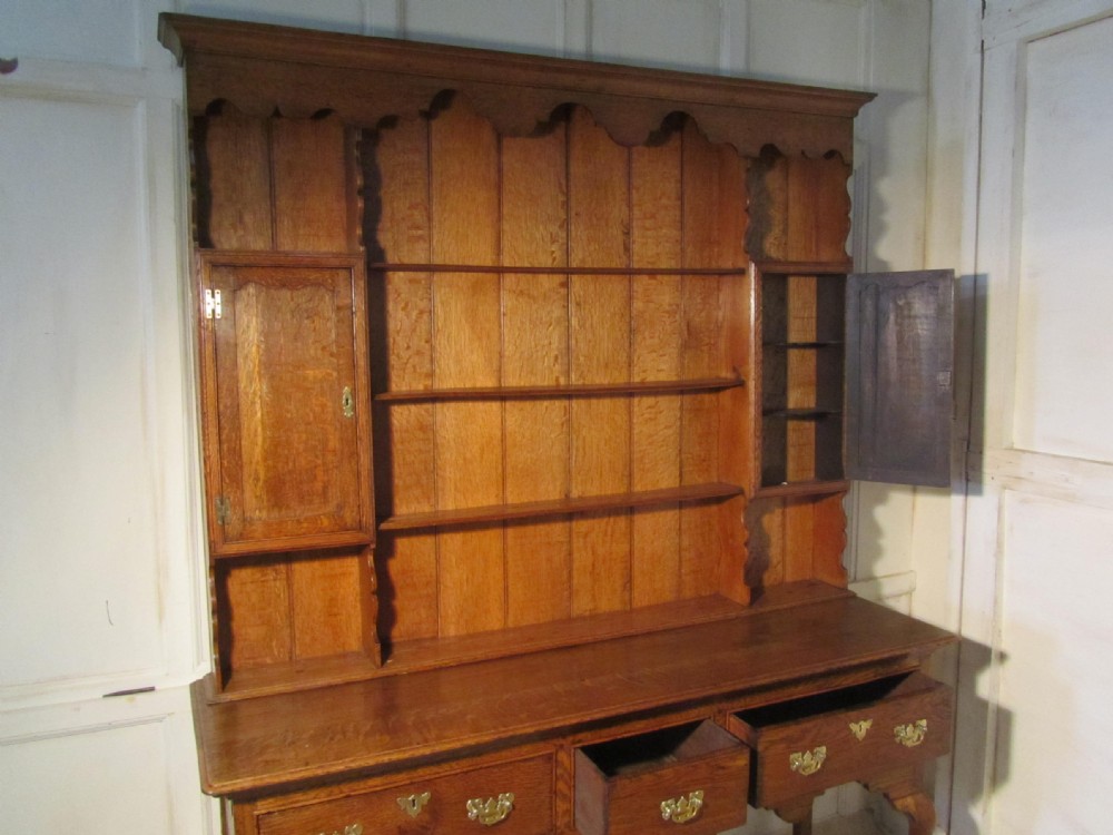 A Georgian country oak dresser with a three-drawer base on cabriole legs, brass hardware, and an open plate rack with small side cupboards. View VII