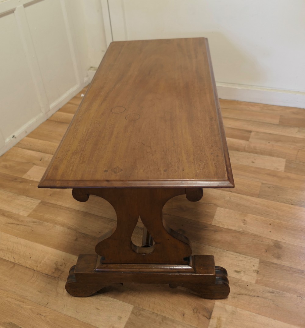 A low rectangular walnut coffee table featuring a flat top with bevelled edges, supported by pierced trestle end legs connected by a central stretcher.