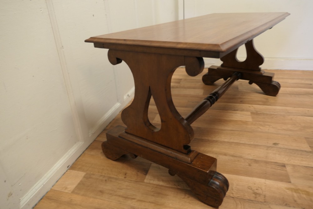 A low rectangular walnut coffee table featuring a flat top with bevelled edges, supported by pierced trestle end legs connected by a central stretcher. View II