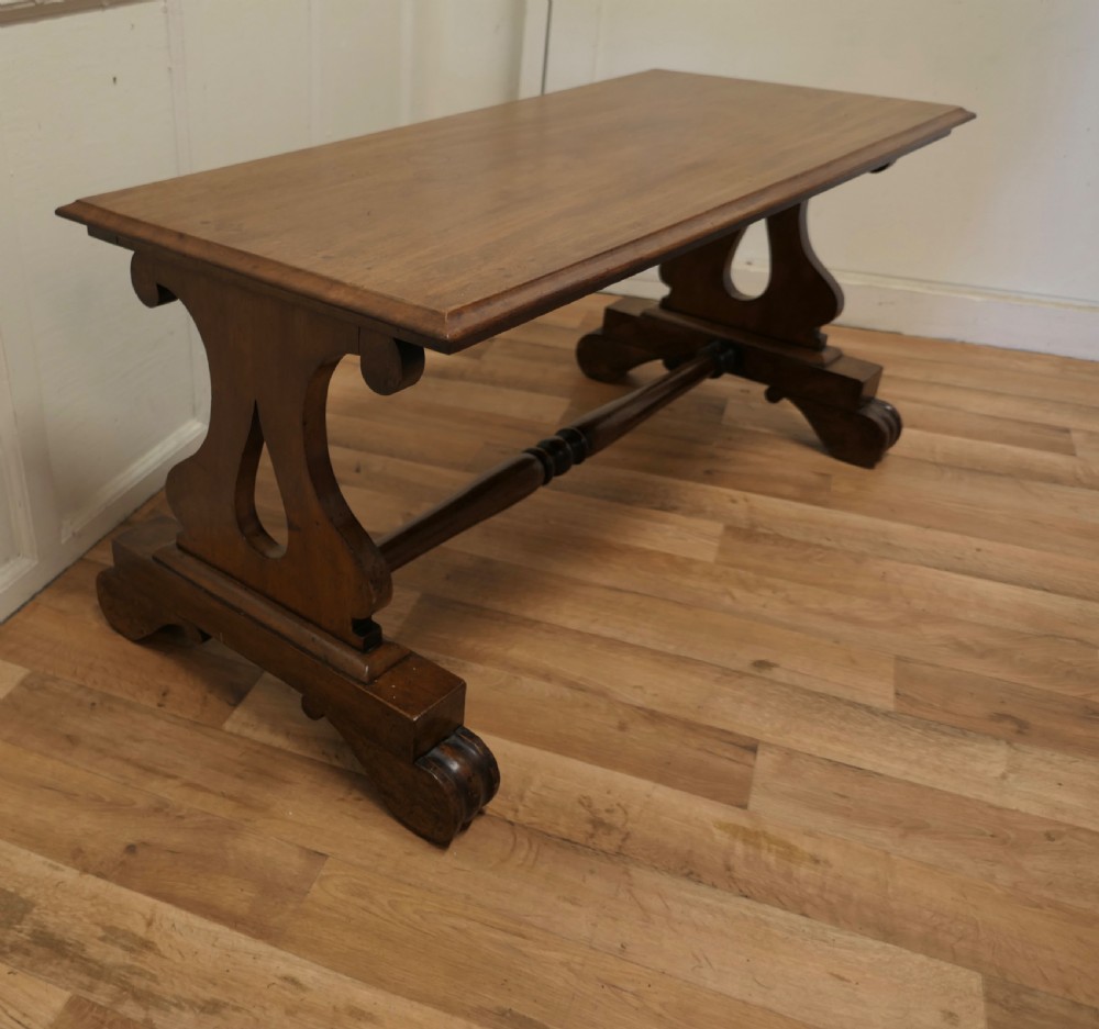 A low rectangular walnut coffee table featuring a flat top with bevelled edges, supported by pierced trestle end legs connected by a central stretcher. View III