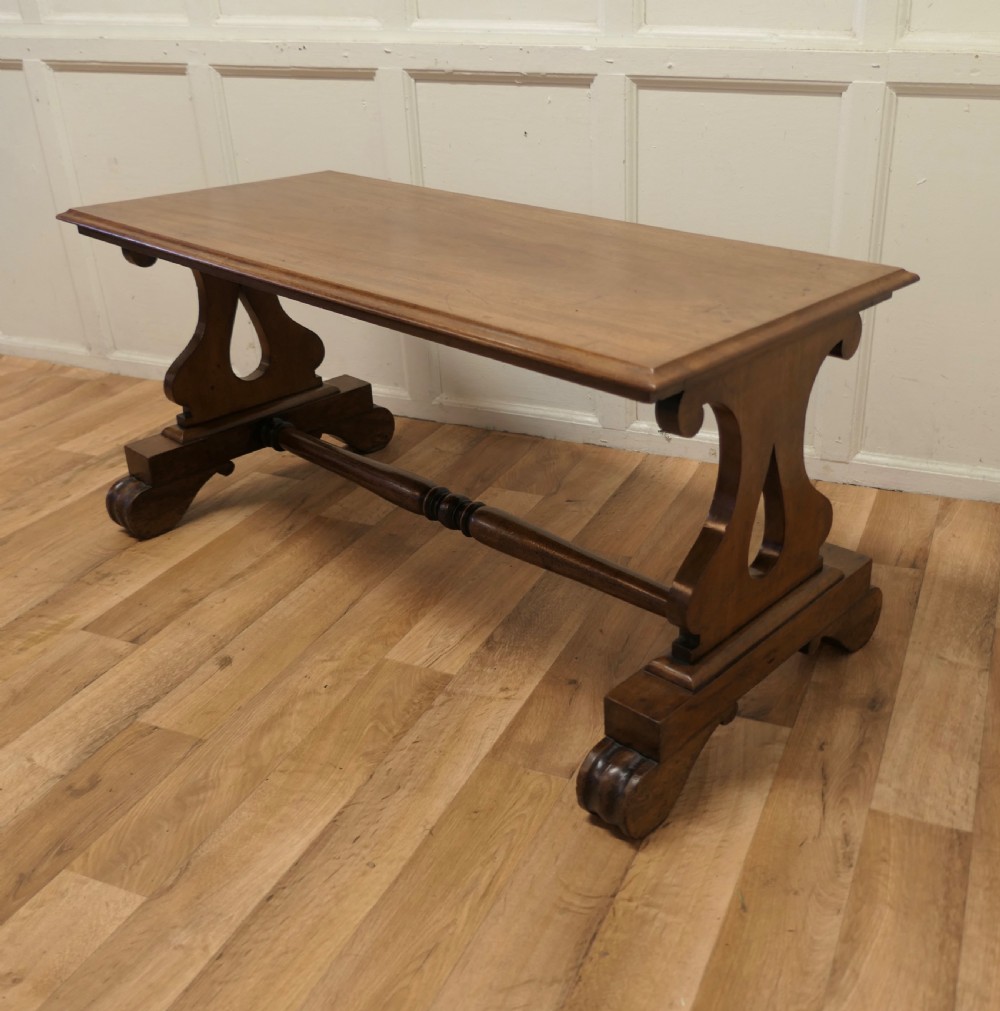A low rectangular walnut coffee table featuring a flat top with bevelled edges, supported by pierced trestle end legs connected by a central stretcher. View V