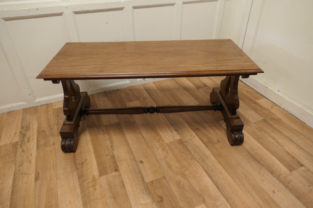 A low rectangular walnut coffee table featuring a flat top with bevelled edges, supported by pierced trestle end legs connected by a central stretcher. View VI