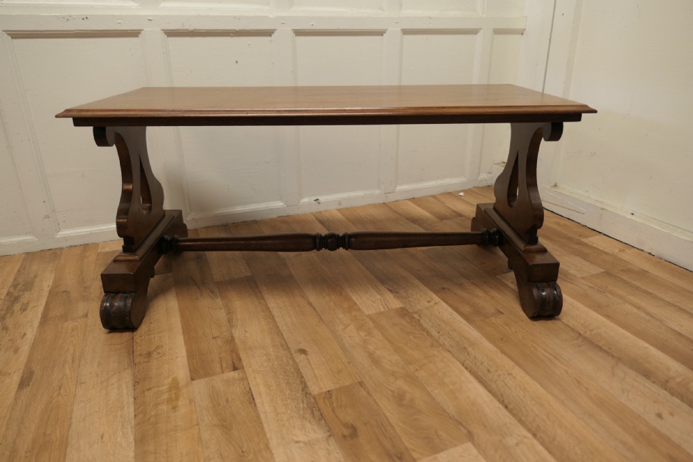 A low rectangular walnut coffee table featuring a flat top with bevelled edges, supported by pierced trestle end legs connected by a central stretcher. View VII