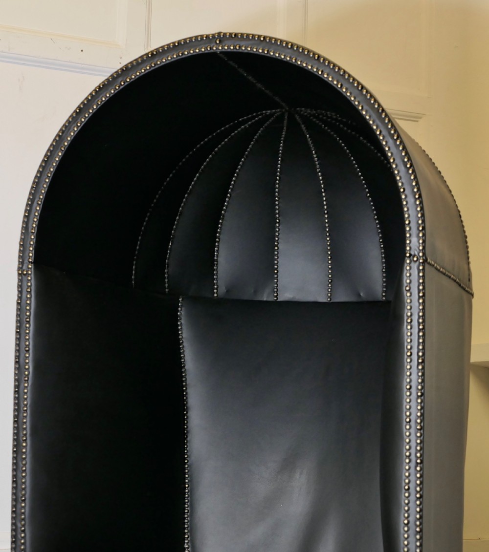 A 19th-century tall hooded hall porter chair upholstered in dark leather with stud trim and a wood base. View VII