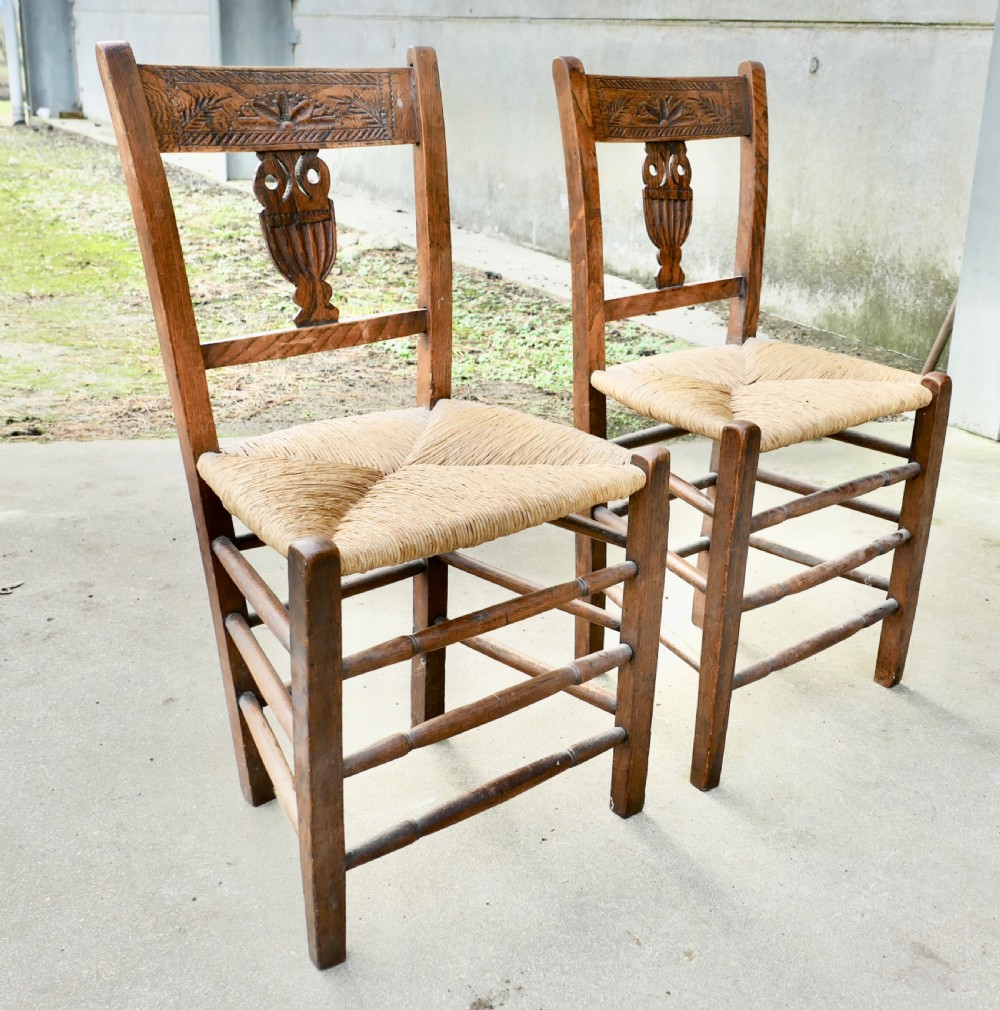 A pair of early 19th-century elm side chairs featuring carved back crests, urn-shaped splats, and woven rush seats.