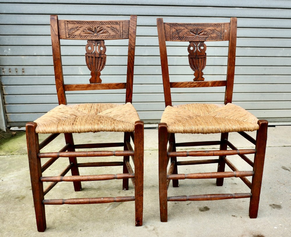 A pair of early 19th-century elm side chairs featuring carved back crests, urn-shaped splats, and woven rush seats. View II