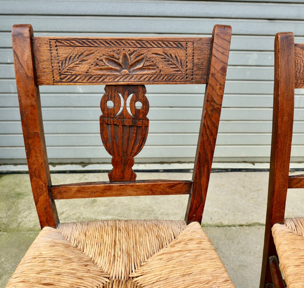 A pair of early 19th-century elm side chairs featuring carved back crests, urn-shaped splats, and woven rush seats. View V