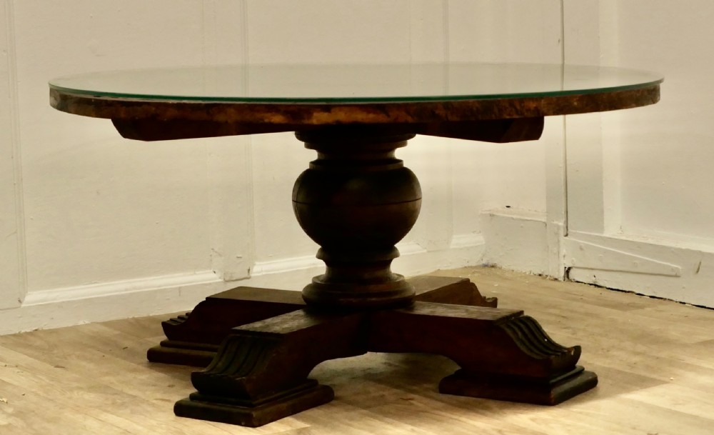 A low circular coffee table made of dark walnut wood featuring a glass top surface, a heavy turned pedestal baluster, and a four-star carved base.