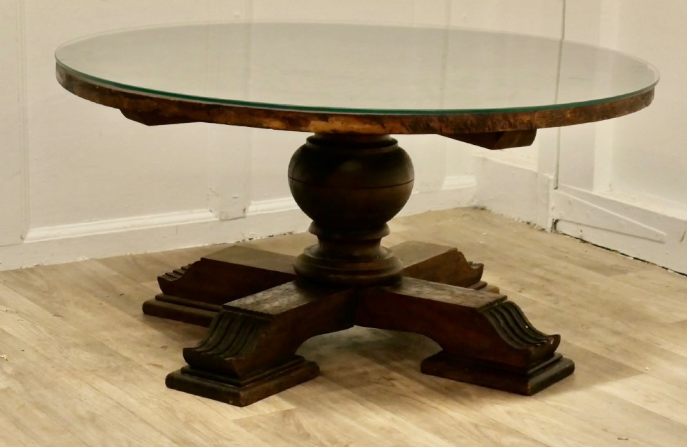 A low circular coffee table made of dark walnut wood featuring a glass top surface, a heavy turned pedestal baluster, and a four-star carved base. View II