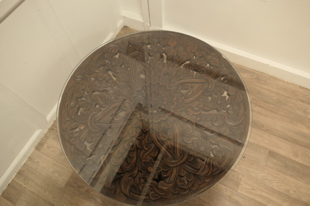 A low circular coffee table made of dark walnut wood featuring a glass top surface, a heavy turned pedestal baluster, and a four-star carved base. View V