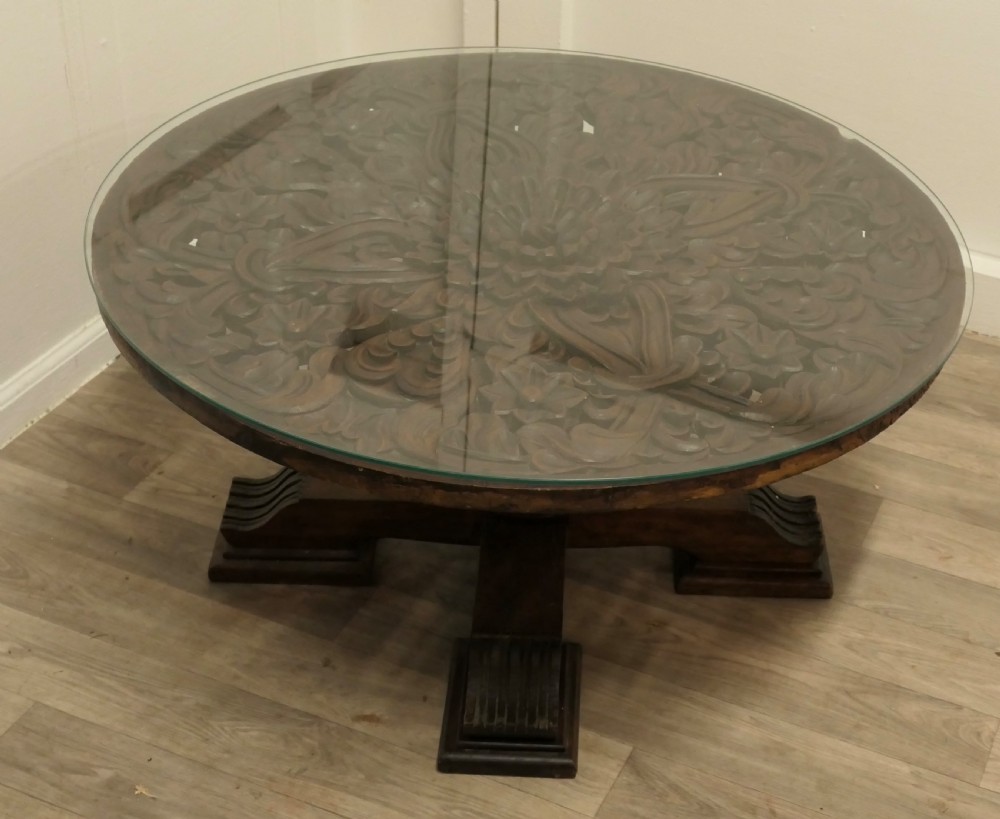 A low circular coffee table made of dark walnut wood featuring a glass top surface, a heavy turned pedestal baluster, and a four-star carved base. View VI